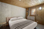 Cozy chalet bedroom with wooden walls and ceiling, featuring a comfortable double bed and a rustic dresser.