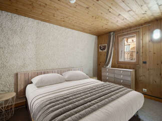 Cozy chalet bedroom with wooden walls and ceiling, featuring a comfortable double bed and a rustic dresser.