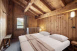 Cozy chalet bedroom with twin beds, wooden walls, and mountain views.