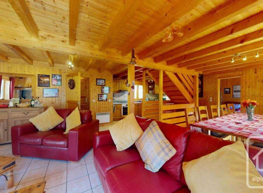 This stunning chalet boasts a spacious open-plan living area with exposed wooden beams, a cozy fireplace, and comfortable red leather sofas.