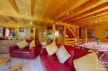 This stunning chalet boasts a spacious open-plan living area with exposed wooden beams, a cozy fireplace, and comfortable red leather sofas.