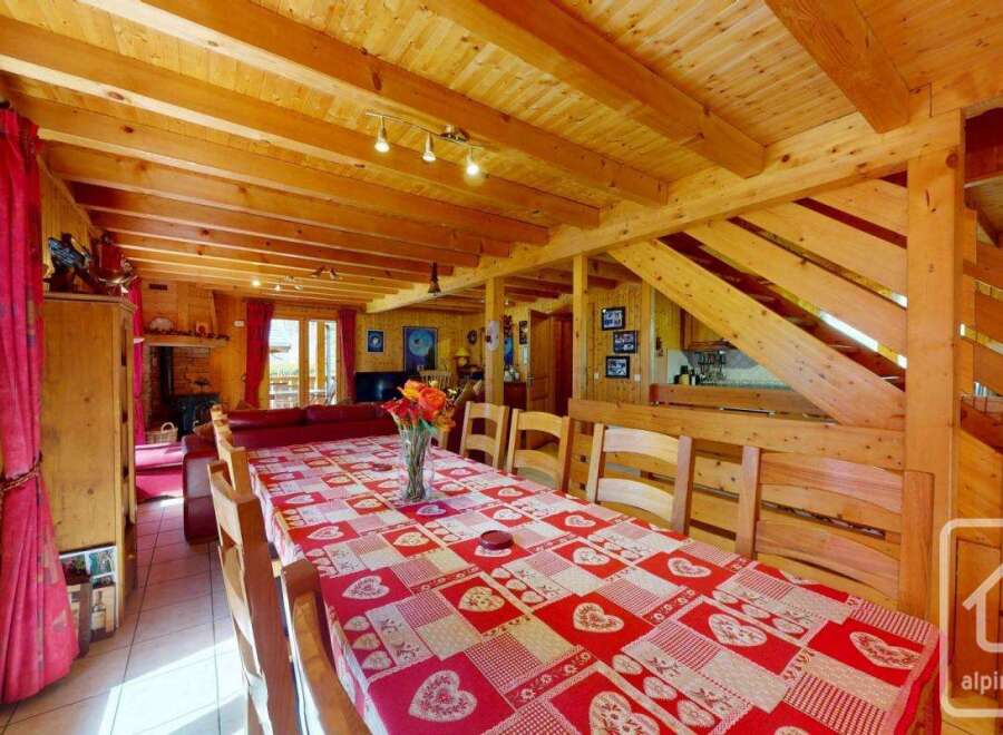 This charming chalet boasts a spacious dining area with a large wooden table perfect for family gatherings, complemented by a warm and inviting living room with a cozy fireplace.