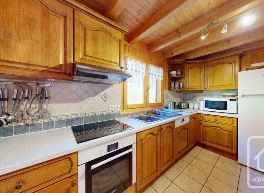 This charming kitchen boasts a rustic wooden design with modern appliances, including a built-in oven and hob, microwave, and refrigerator.