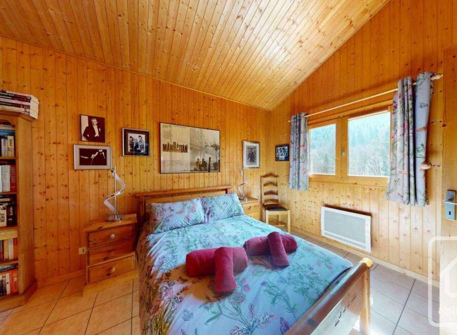 Cozy chalet bedroom with wooden walls and a double bed, featuring a bookshelf filled with books and framed movie posters.