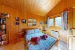 Cozy chalet bedroom with wooden walls and a double bed, featuring a bookshelf filled with books and framed movie posters.