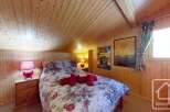 Cosy chalet bedroom with floral bedding, wooden walls and ceiling, and a window with curtains.
