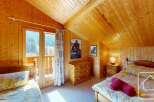 Cosy chalet bedroom with twin beds, wooden walls and ceilings, and a balcony offering stunning mountain views.
