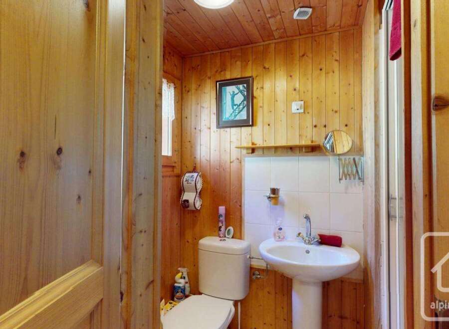 Cozy chalet bathroom with wood paneling, featuring a toilet, sink, and shower.