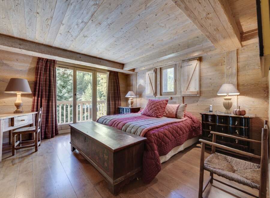 Rustic mountain chalet bedroom with wooden walls and ceilings, featuring a cozy bed with a red quilt and antique wooden furniture.