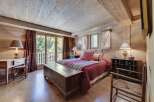 Rustic mountain chalet bedroom with wooden walls and ceilings, featuring a cozy bed with a red quilt and antique wooden furniture.