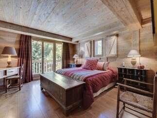 Rustic mountain chalet bedroom with wooden walls and ceilings, featuring a cozy bed with a red quilt and antique wooden furniture.