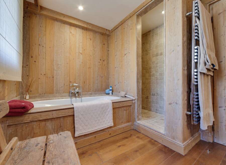 This luxurious bathroom boasts a rustic-chic design with wood paneling, a freestanding bathtub, and a separate shower.