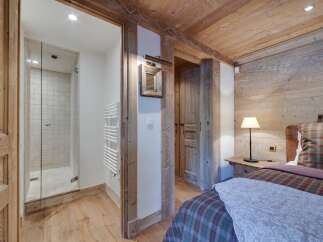 Rustic-chic bedroom with exposed wood beams and walls, featuring a cozy plaid bedspread and a modern ensuite bathroom with glass shower enclosure.