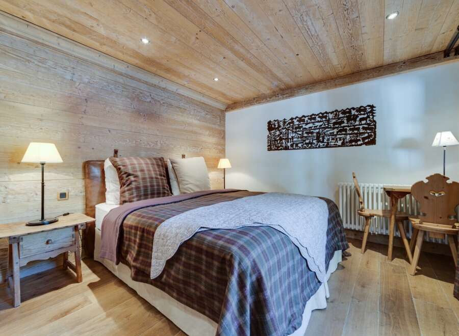 Cozy chalet bedroom with wooden walls and ceiling, featuring a comfortable double bed with plaid bedding.