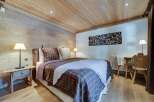 Cozy chalet bedroom with wooden walls and ceiling, featuring a comfortable double bed with plaid bedding.