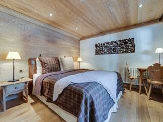 Cozy chalet bedroom with wooden walls and ceiling, featuring a comfortable double bed with plaid bedding.