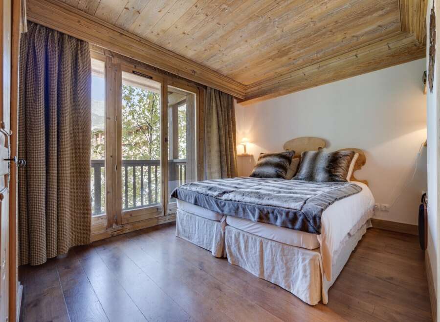 Cozy chalet bedroom with wooden beams, hardwood floors, and a balcony offering stunning views.