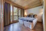 Cozy chalet bedroom with wooden beams, hardwood floors, and a balcony offering stunning views.