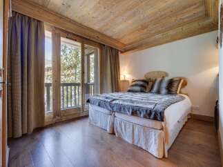 Cozy chalet bedroom with wooden beams, hardwood floors, and a balcony offering stunning views.