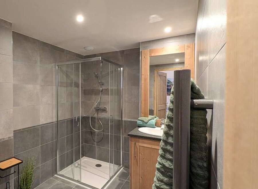 This stunning bathroom boasts modern gray tile, a spacious walk-in shower, and a sleek wooden vanity.
