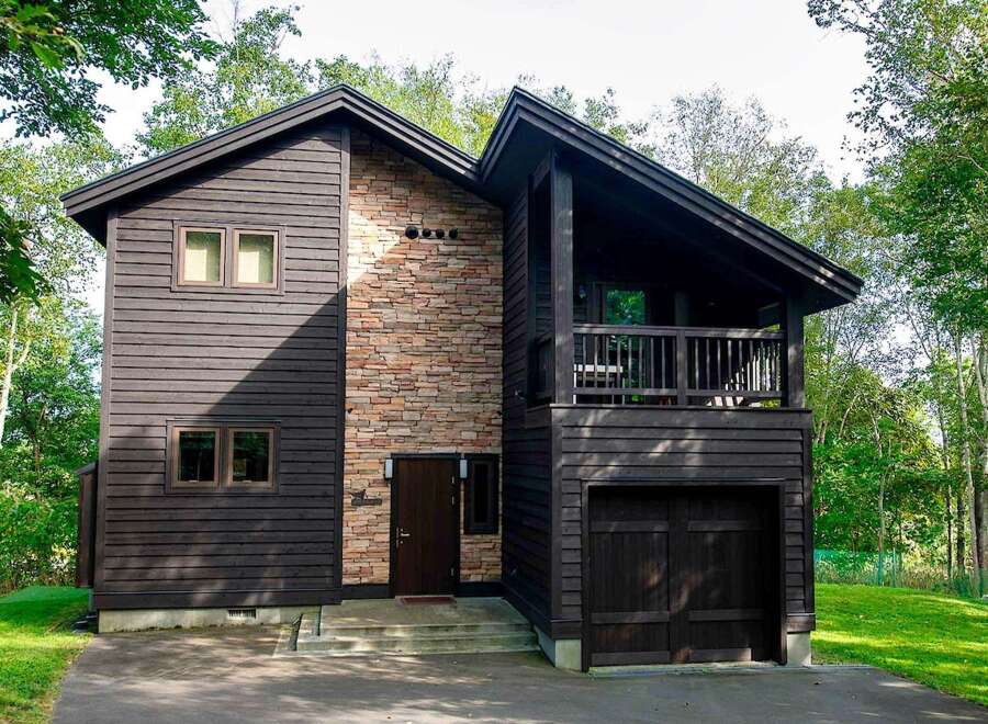 This stunning two-story home boasts a unique architectural design, featuring a blend of dark wood siding and a striking stone accent wall.