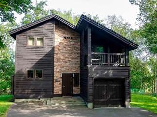 This stunning two-story home boasts a unique architectural design, featuring a blend of dark wood siding and a striking stone accent wall.
