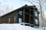 This stunning modern chalet boasts a dark wood exterior, large windows offering breathtaking views, and a spacious deck perfect for enjoying the snowy landscape.