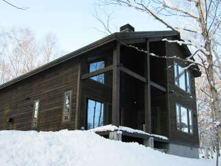 This stunning modern chalet boasts a dark wood exterior, large windows offering breathtaking views, and a spacious deck perfect for enjoying the snowy landscape.