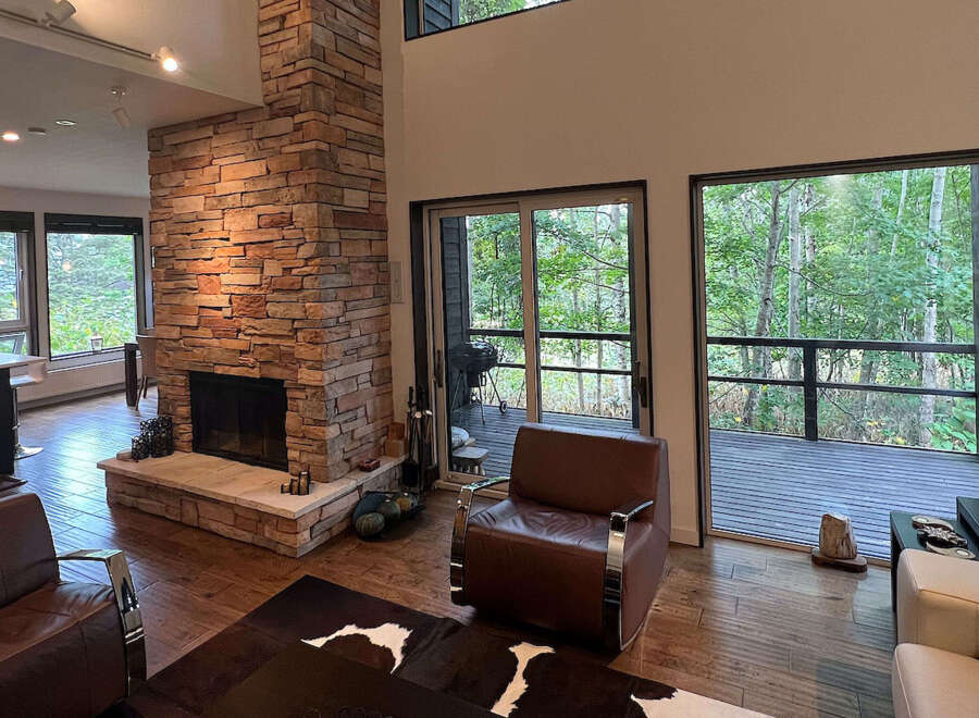 This stunning home boasts an open floor plan with hardwood floors, a cozy stone fireplace, and large windows offering breathtaking views of the surrounding forest.