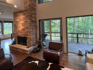 This stunning home boasts an open floor plan with hardwood floors, a cozy stone fireplace, and large windows offering breathtaking views of the surrounding forest.