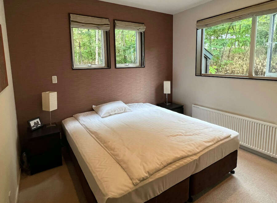 Cozy bedroom with a double bed, two windows offering forest views, and a modern aesthetic.