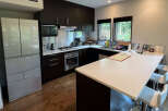 This modern kitchen boasts sleek dark brown cabinetry, stainless steel appliances, and a spacious island with seating.