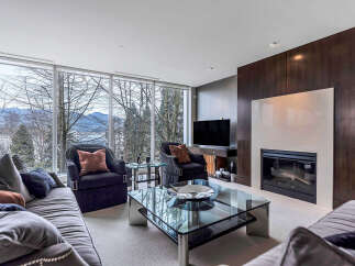 This luxurious living room boasts stunning views of mountains and water through expansive windows, creating a serene and inviting atmosphere.