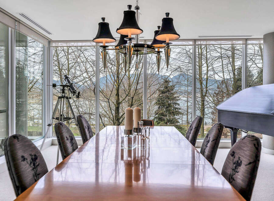 This luxurious dining room boasts floor-to-ceiling windows offering breathtaking views of the water and mountains, creating a serene and elegant atmosphere.