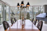 This luxurious dining room boasts floor-to-ceiling windows offering breathtaking views of the water and mountains, creating a serene and elegant atmosphere.