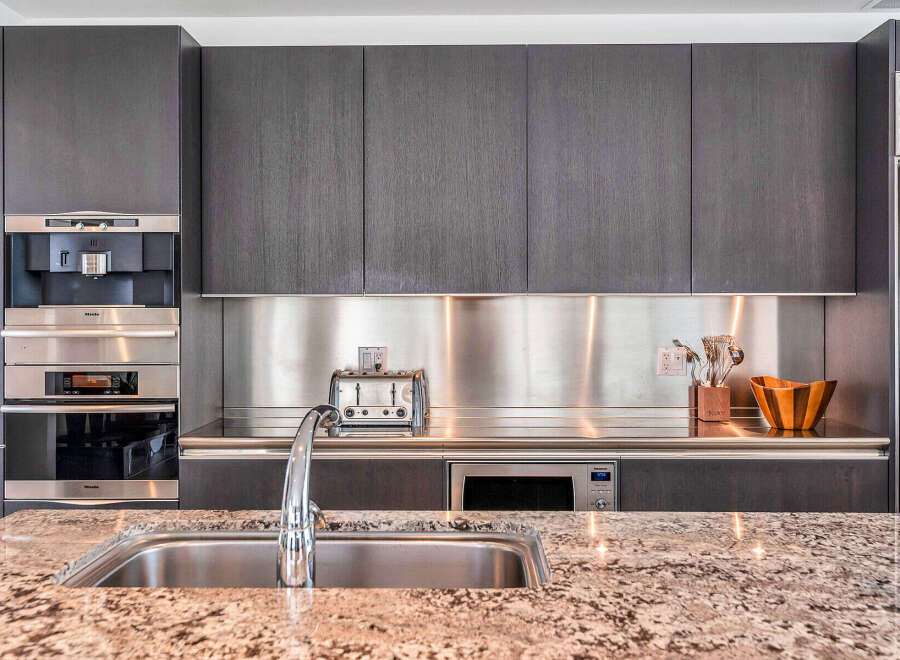 This stunning kitchen boasts sleek dark gray cabinetry, complemented by stainless steel countertops and backsplash.