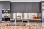 This stunning kitchen boasts sleek dark gray cabinetry, complemented by stainless steel countertops and backsplash.