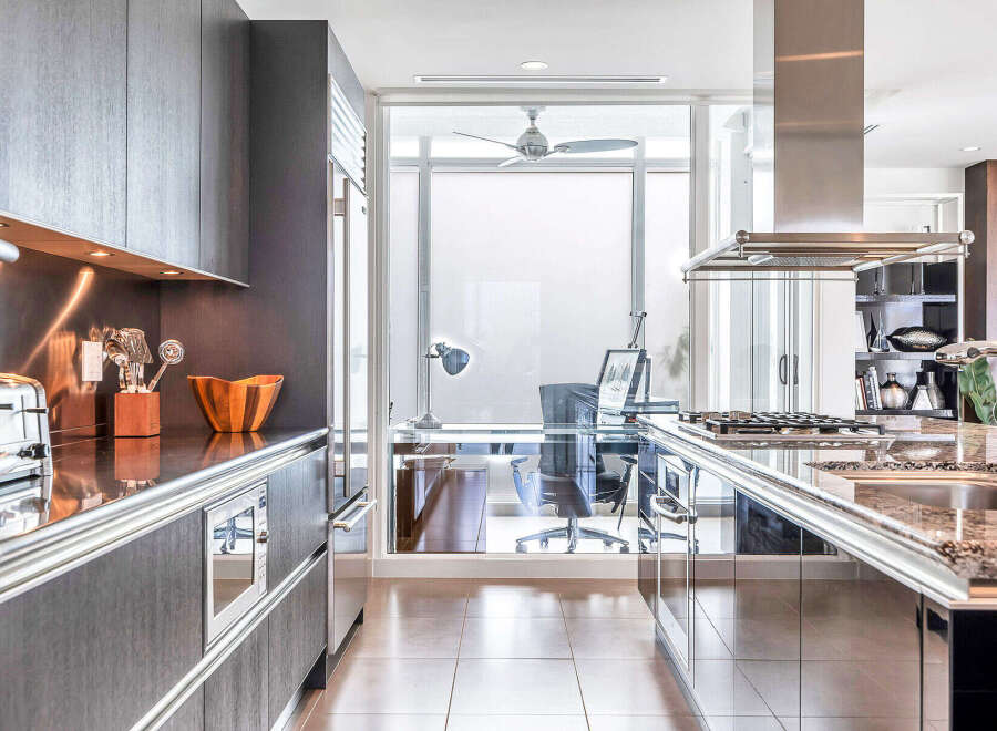 This stunning kitchen boasts sleek, dark gray cabinetry with stainless steel accents, complemented by granite countertops and high-end appliances.