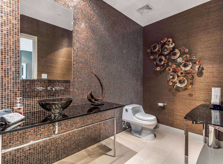 This luxurious powder room boasts a stunning design with dark brown mosaic tile, a sleek glass sink, and modern fixtures.
