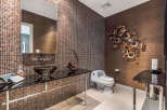 This luxurious powder room boasts a stunning design with dark brown mosaic tile, a sleek glass sink, and modern fixtures.