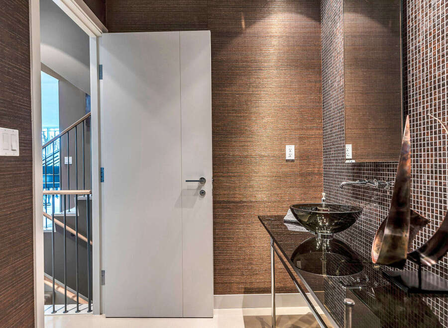 This modern powder room boasts a sleek glass vanity with a unique vessel sink, complemented by dark brown mosaic tile and textured wallpaper.