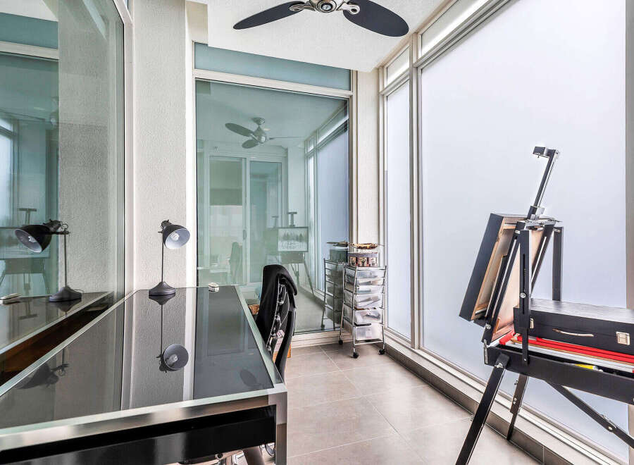 This sun-drenched balcony boasts a versatile workspace, complete with a sleek glass desk, modern lamps, and ample storage.