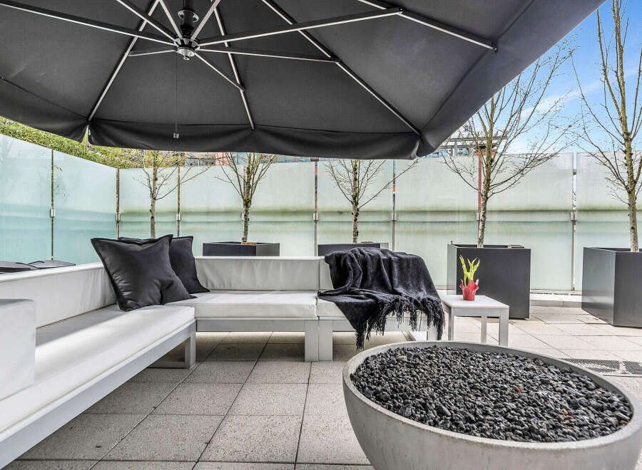This luxurious outdoor patio features a modern sectional sofa with plush cushions, a stylish fire pit, and a large umbrella for shade.