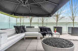 This luxurious outdoor patio features a modern sectional sofa with plush cushions, a stylish fire pit, and a large umbrella for shade.
