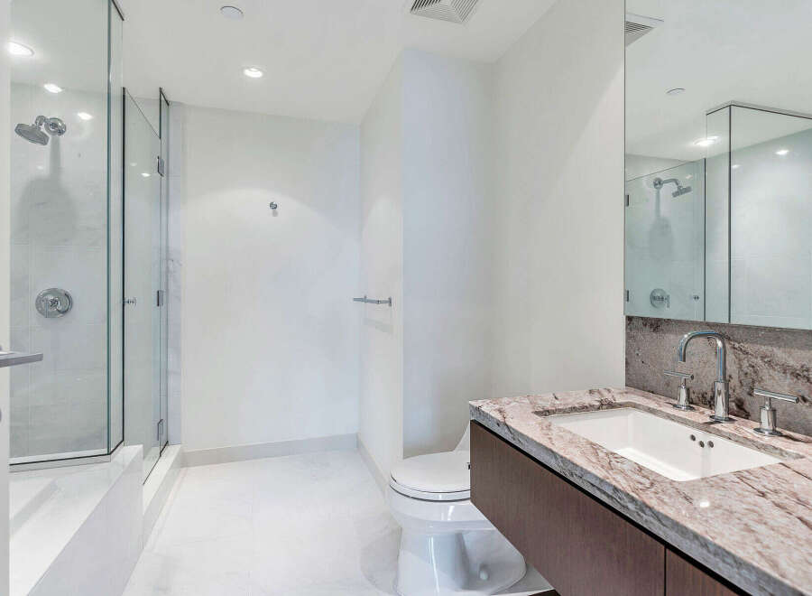 This modern bathroom boasts a spacious walk-in shower with glass enclosure, complemented by a sleek granite countertop vanity with a rectangular undermount sink.