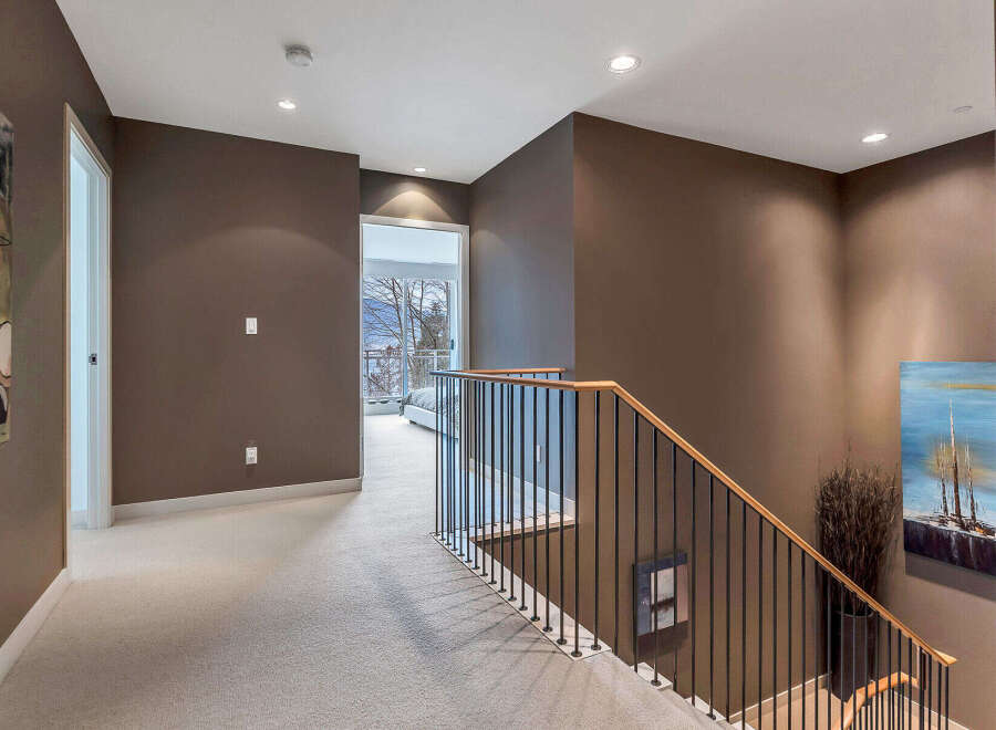 This stunning hallway boasts a modern design with dark brown walls, plush carpeting, and a sleek metal and wood staircase.