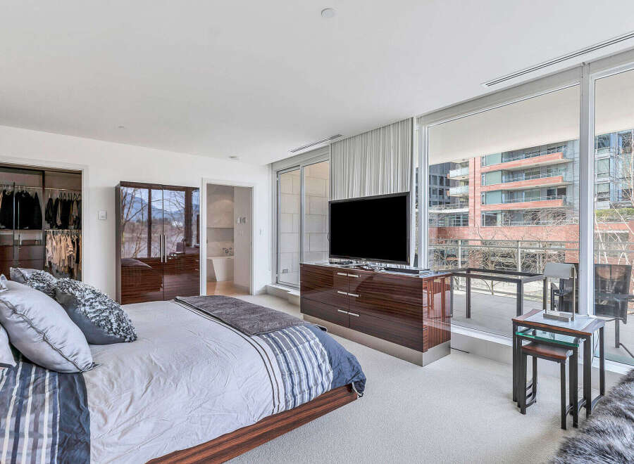 Luxurious bedroom with floor-to-ceiling windows offering stunning city views, a spacious walk-in closet, and a modern ensuite bathroom.