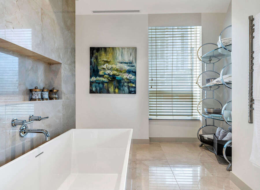 Luxurious bathroom boasts a freestanding bathtub, marble flooring and walls, and a stylish glass shelving unit.