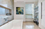 Luxurious bathroom boasts a freestanding bathtub, marble flooring and walls, and a stylish glass shelving unit.