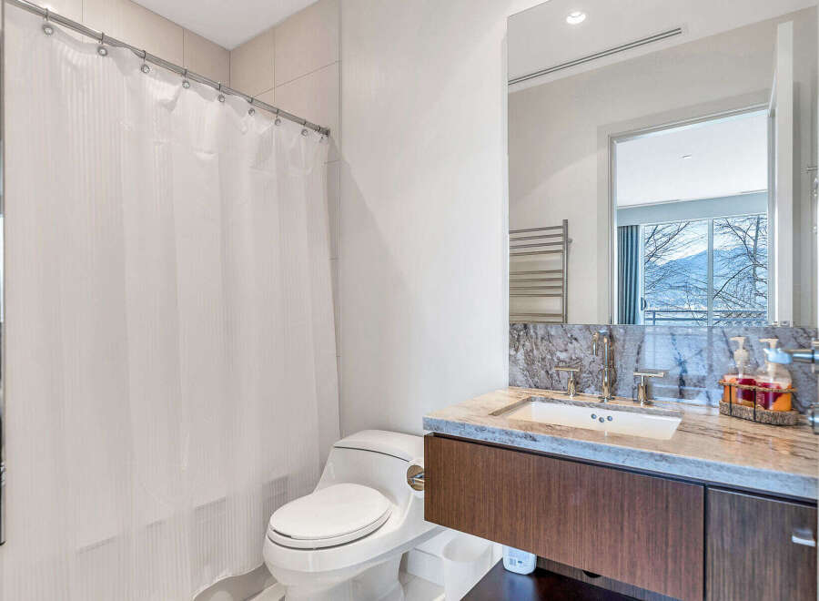 This modern bathroom boasts a sleek design with granite countertops, a contemporary vanity, and a spacious shower with a white curtain.